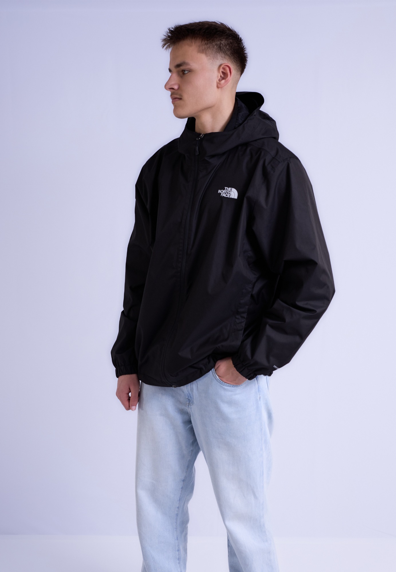 Junger Mann in schwarzer Jacke und hellblauen Jeans, seitlich stehend.