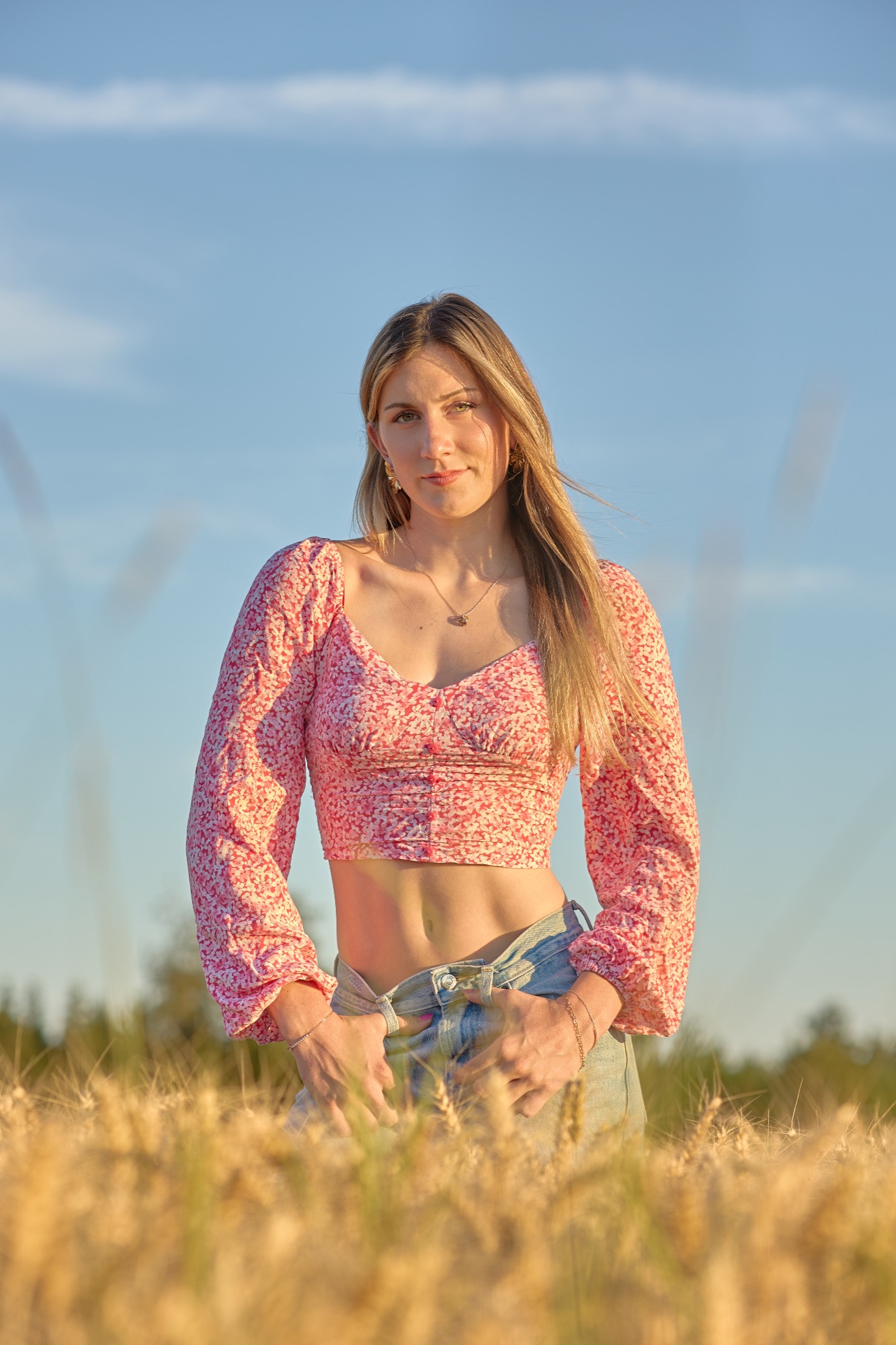 Junge Frau in einem Feld, trägt ein bauchfreies Oberteil und blickt in die Kamera.