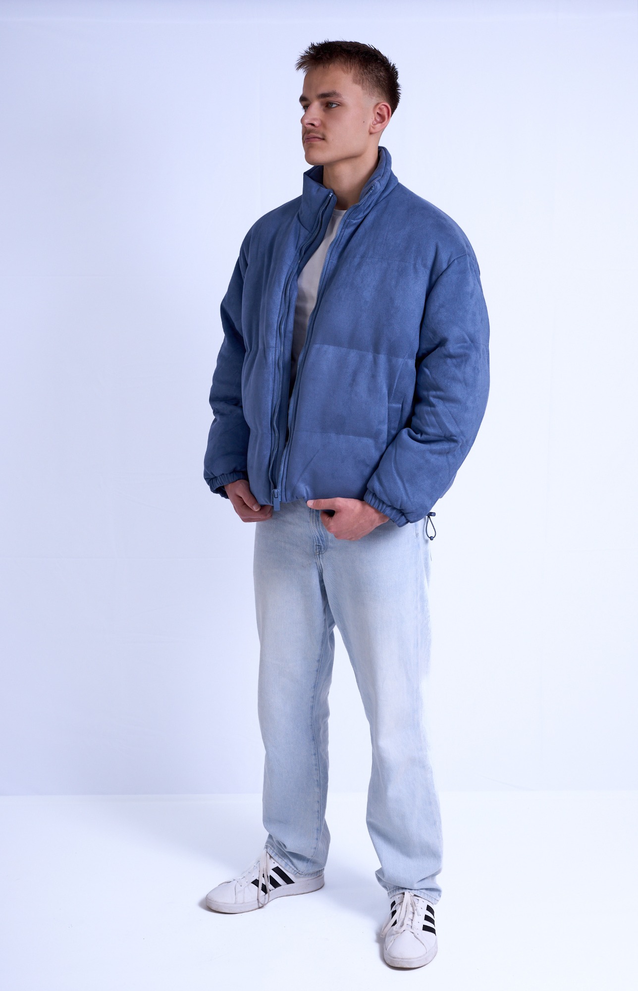 Mann in blauer Jacke und hellen Jeans, steht vor einem neutralen Hintergrund.