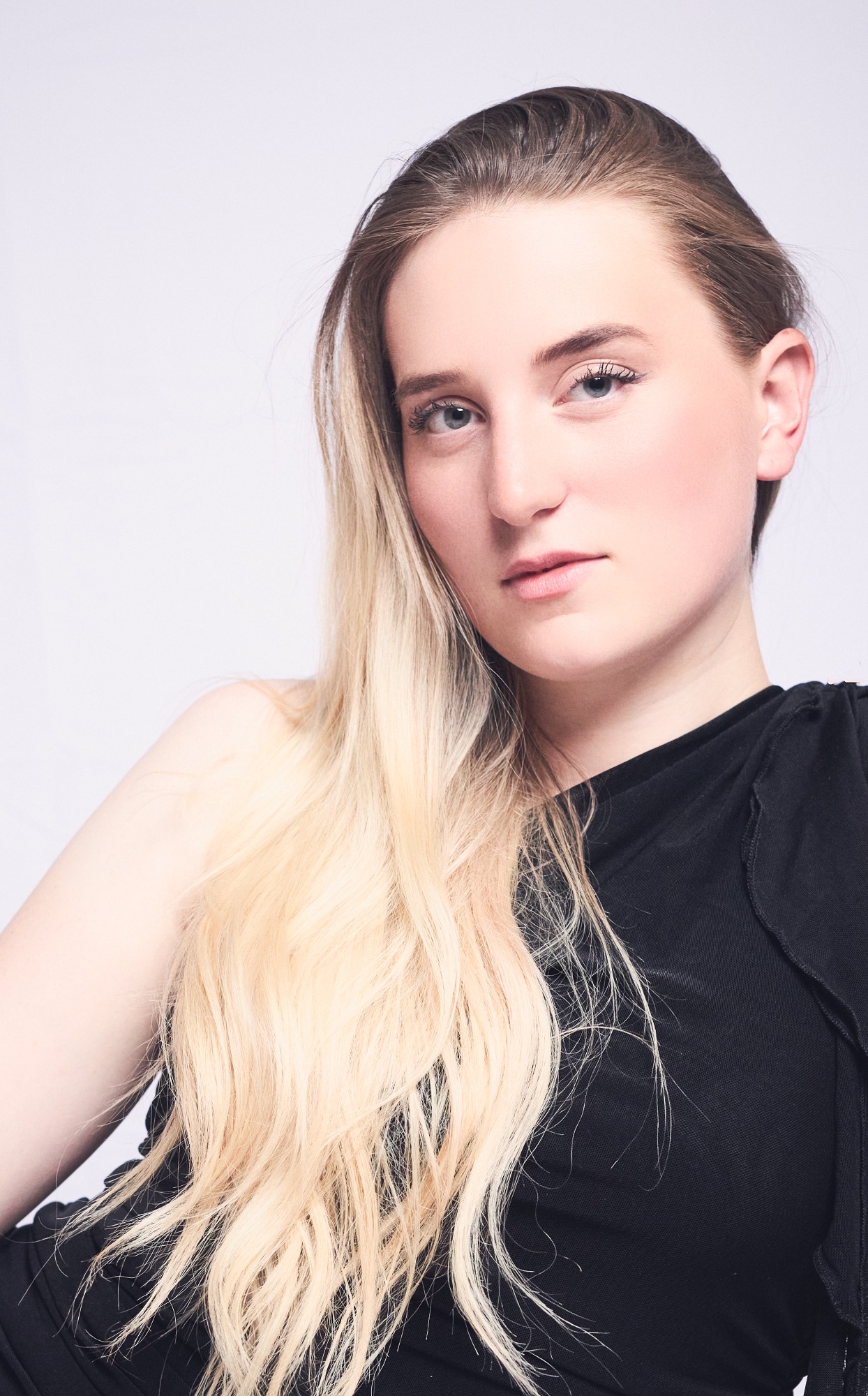 Junge Frau mit langen, blonden Haaren und schwarzem Oberteil, ernsthaft schauend.
