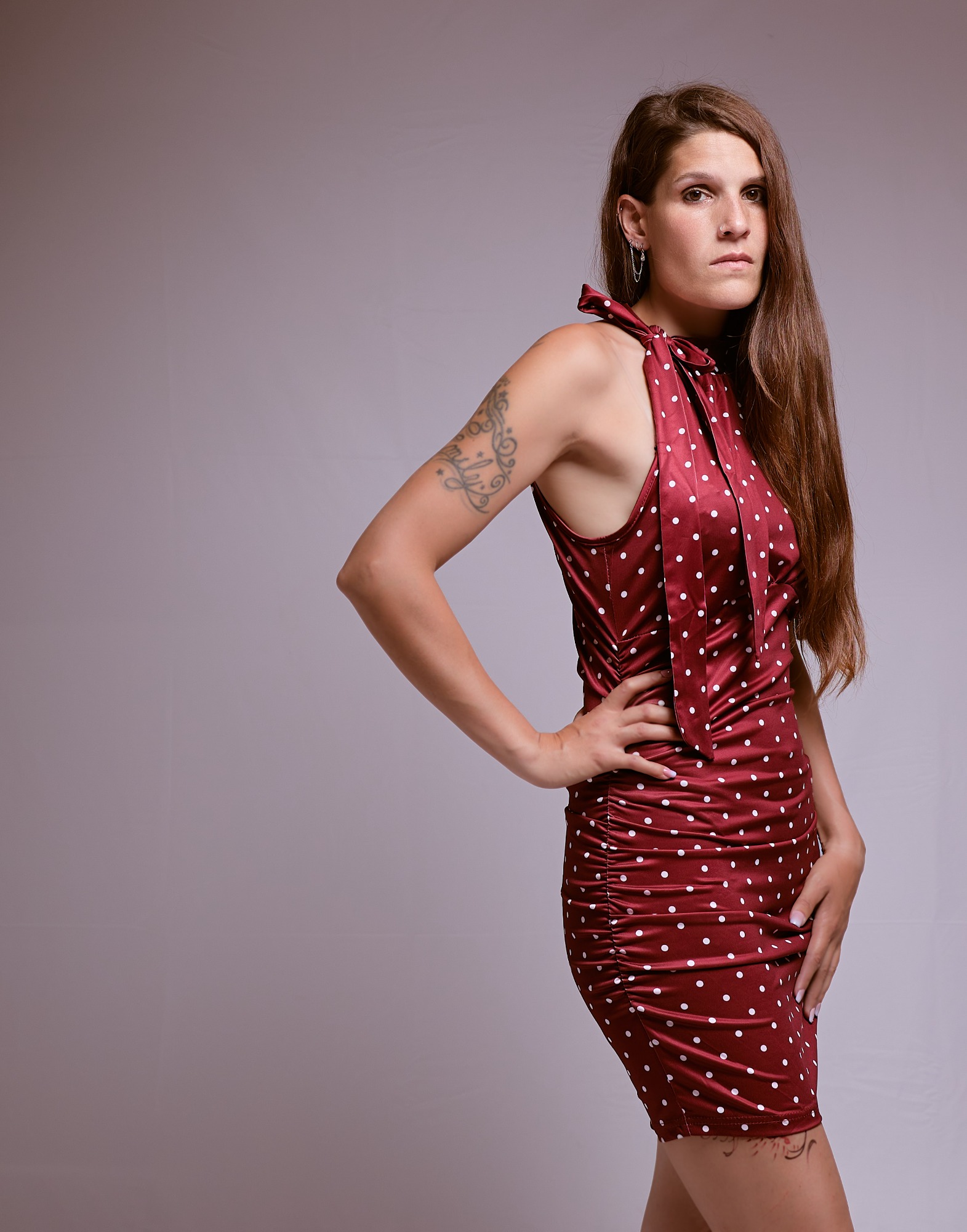 Frau in einem roten, gepunkteten Kleid mit langen Haaren und tätowiertem Arm.
