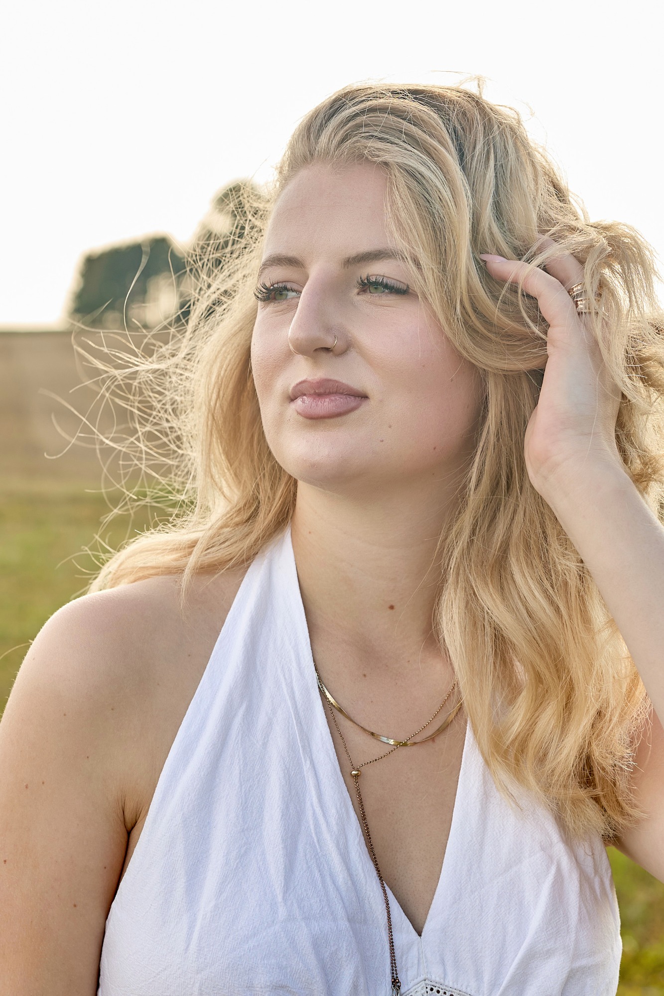 Eine blonde Frau mit lockigem Haar trägt ein weißes Top und schaut nachdenklich.