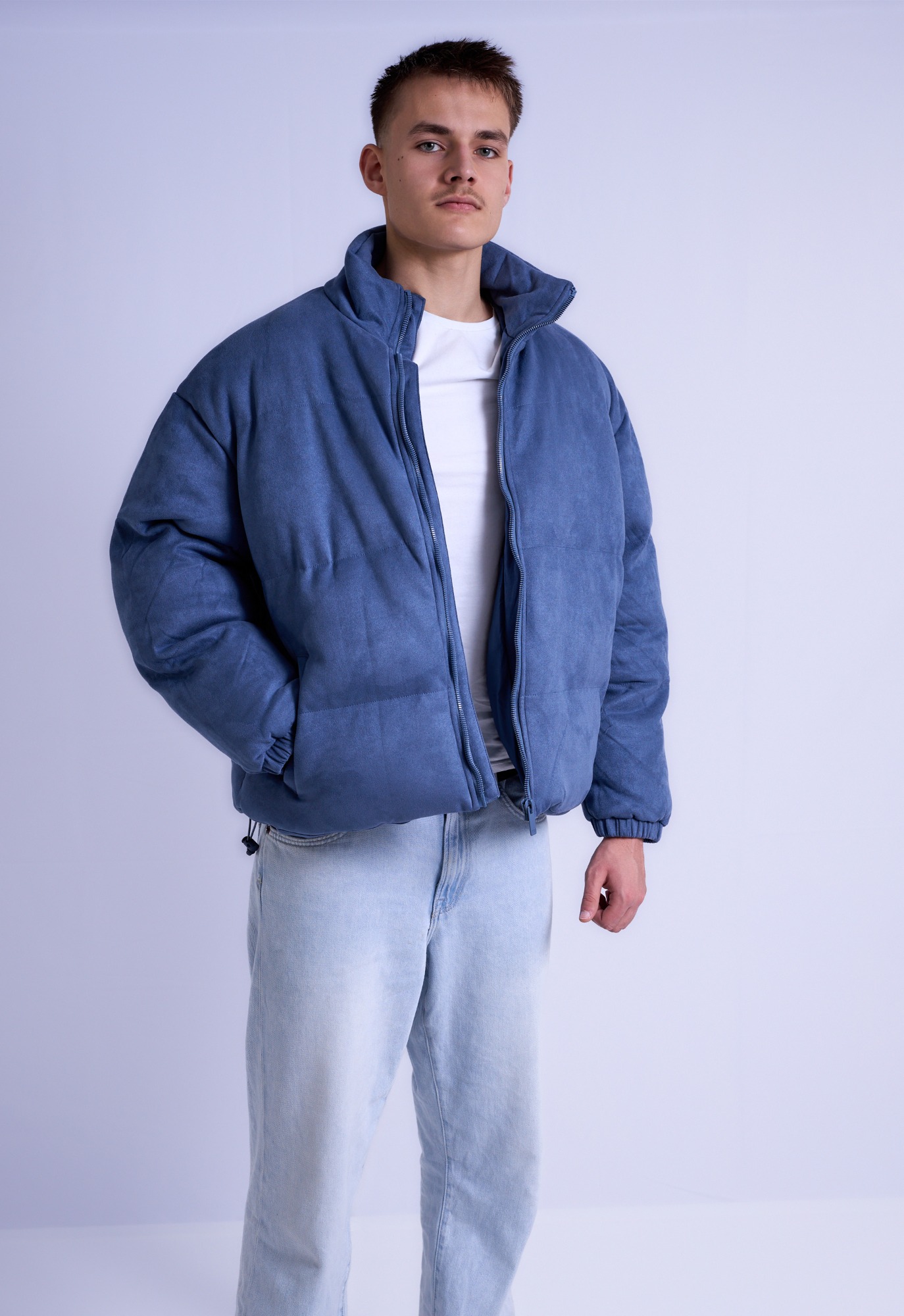 Mann trägt eine bequeme, blaue Daunenjacke und hellblaue Jeans.