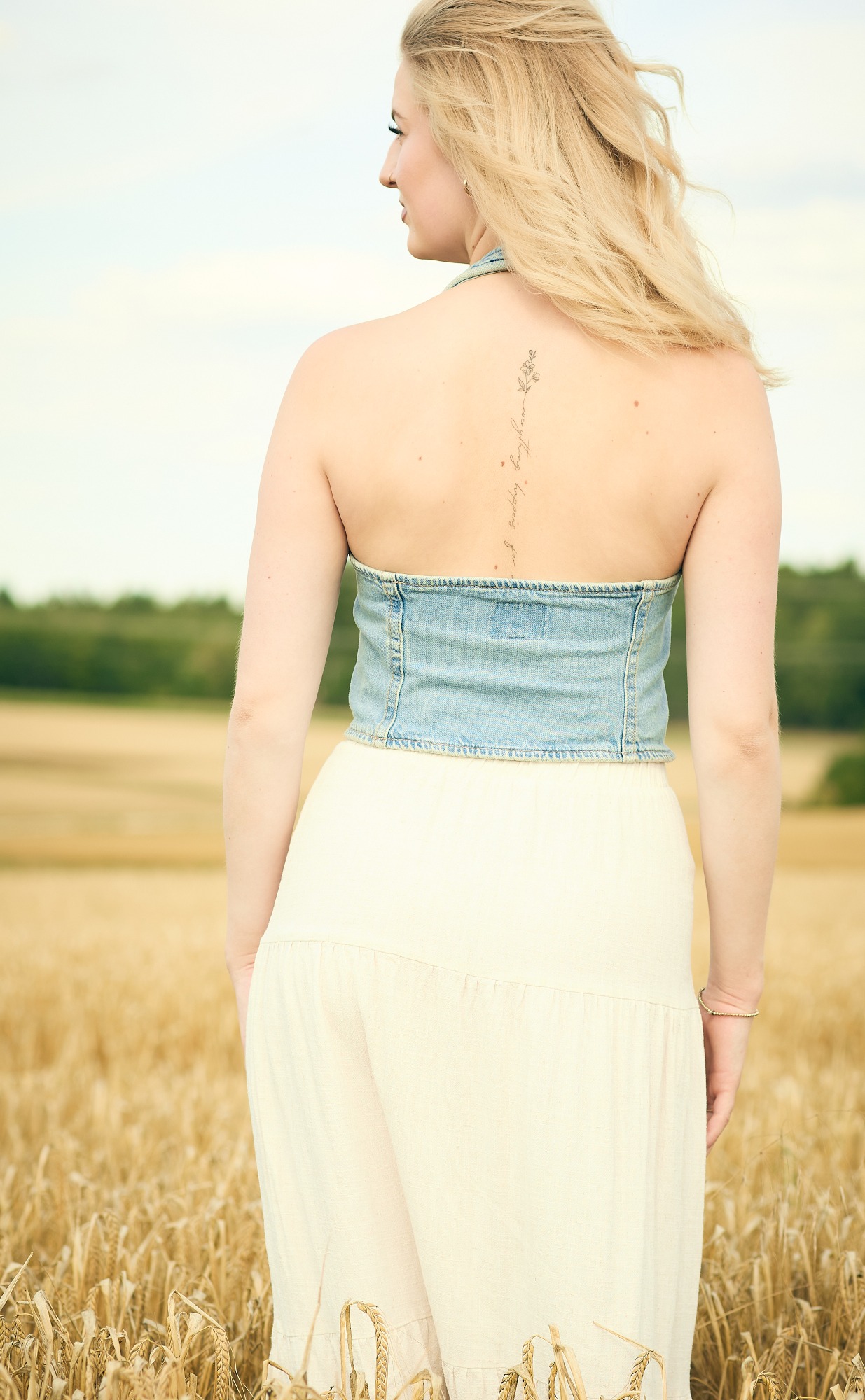 Frau mit blonden Haaren, Rückenansicht, in einem Feld mit reifem Getreide.
