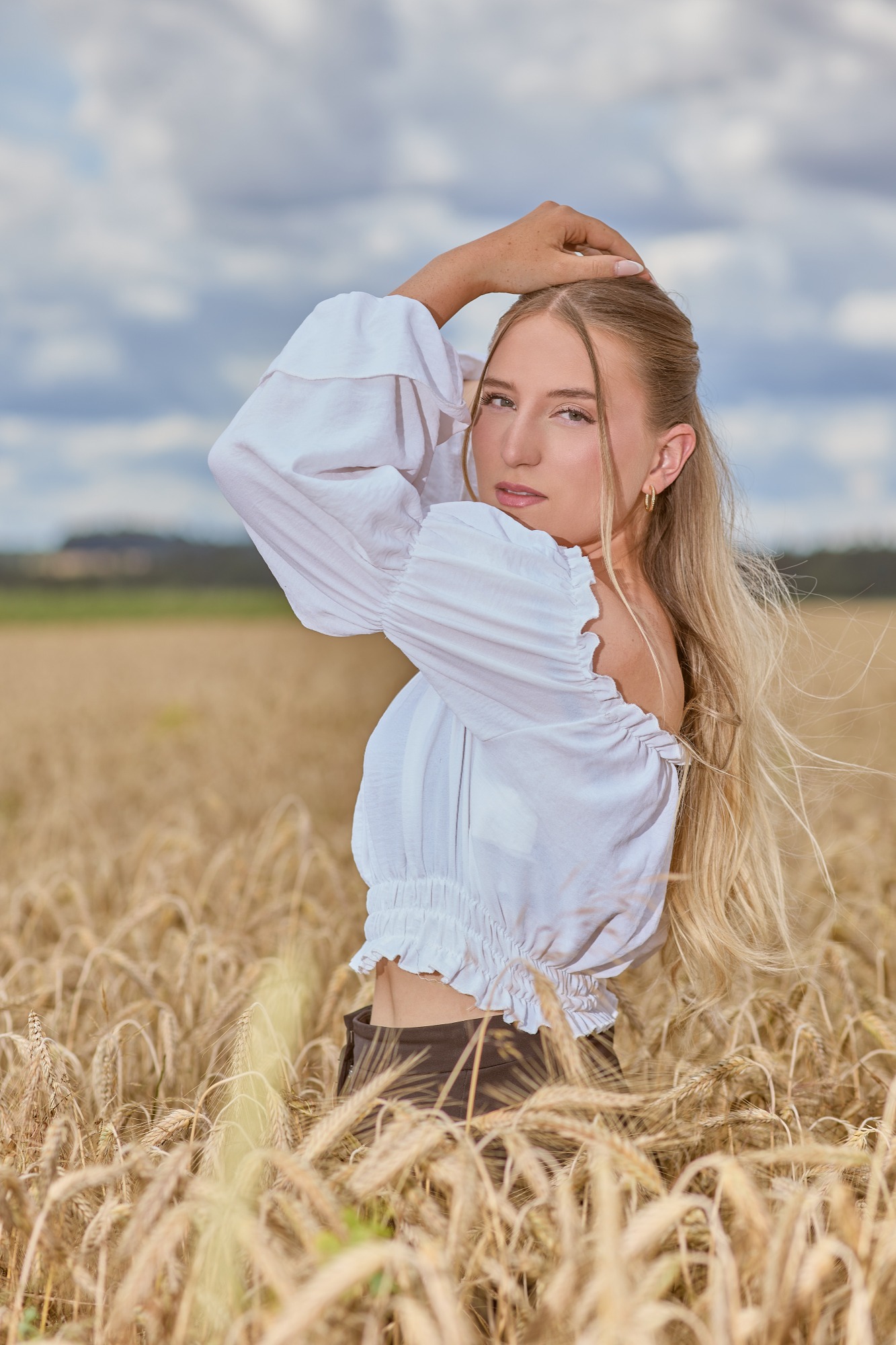 Frau mit blonden Haaren trägt eine weiße Bluse, steht in einem Weizenfeld.