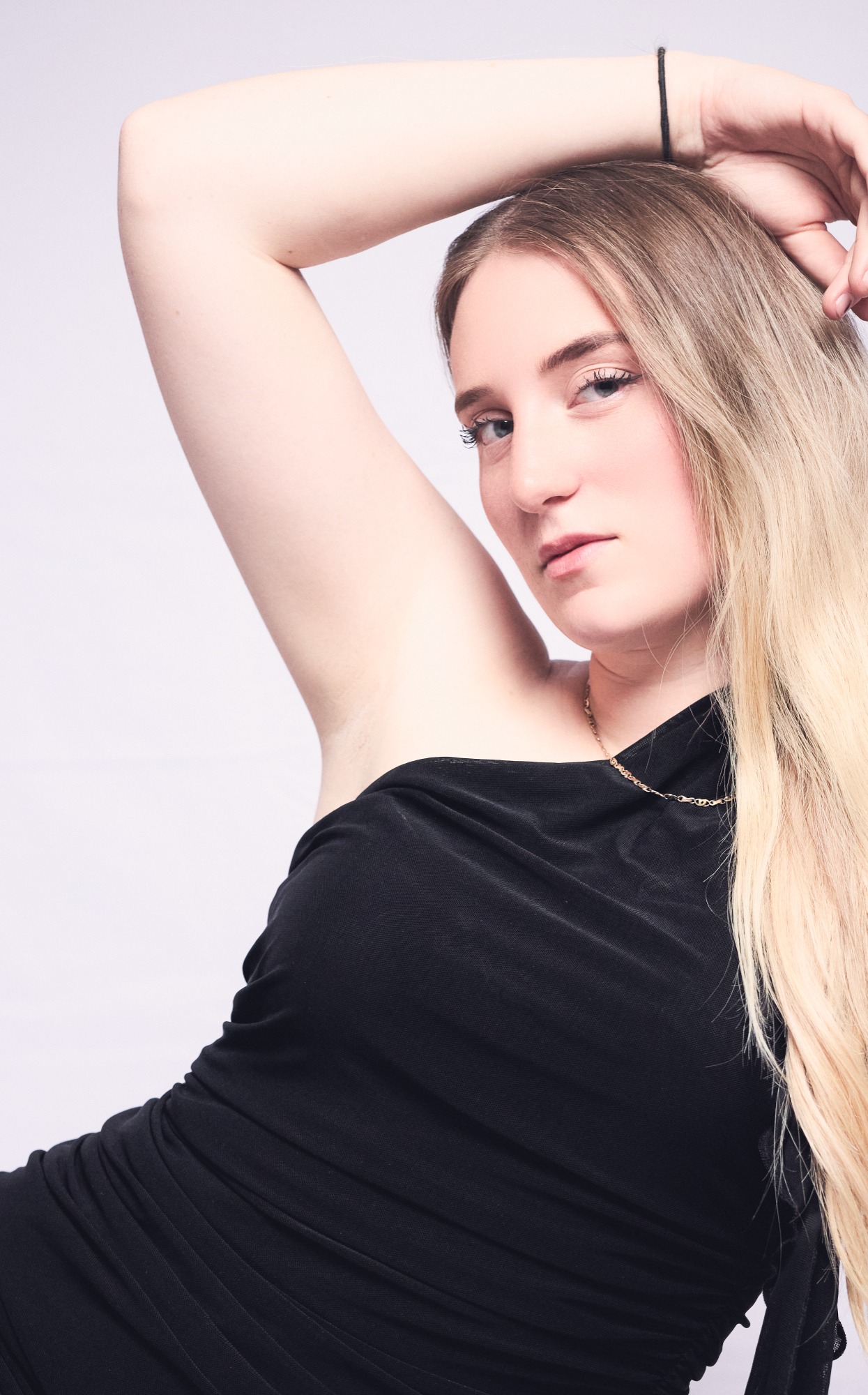 Eine Person mit langen, blonden Haaren trägt ein schwarzes Top und posiert nachdenklich.